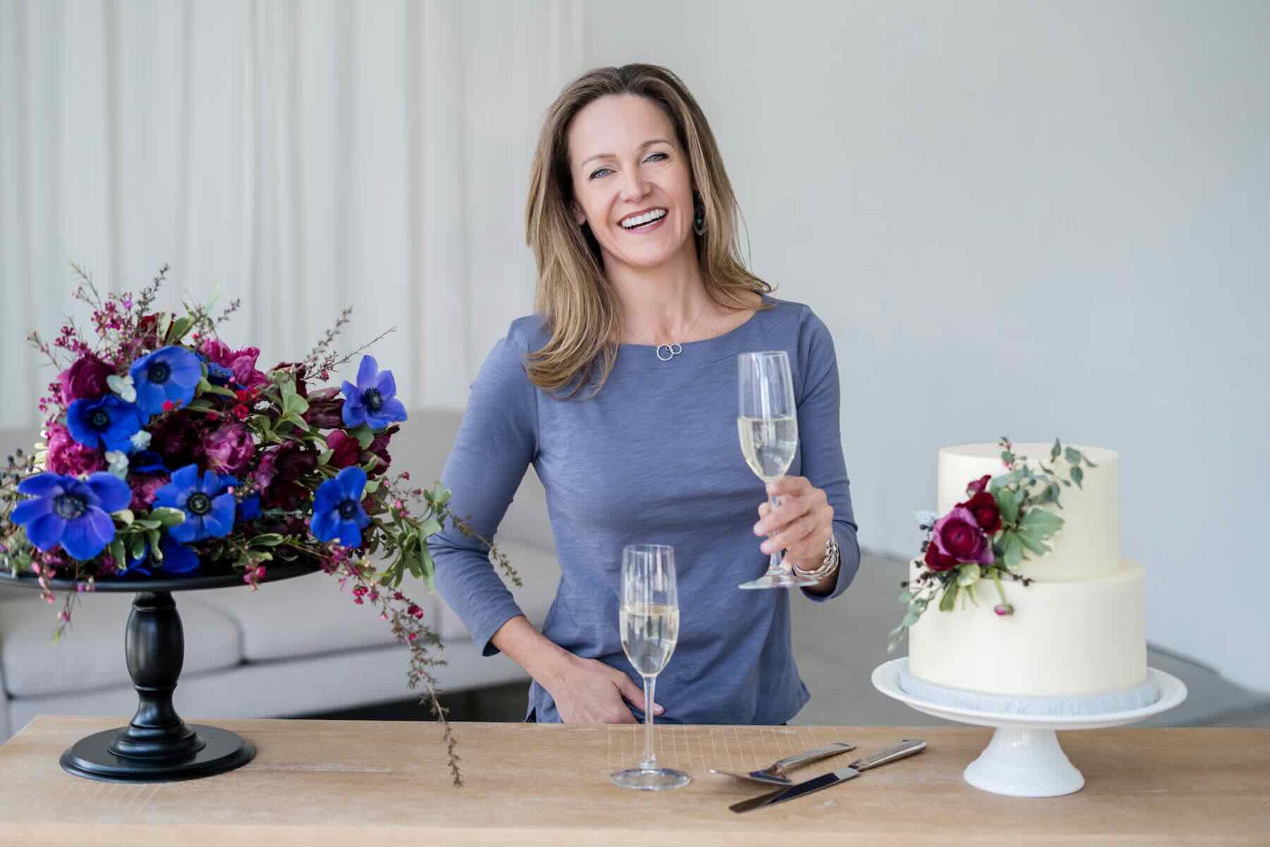 Wendee Vezzetti laughing and raising a glass of champagne beside a wedding cake
