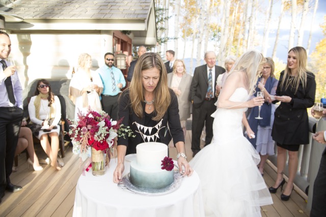 Wendee Vezzetti smiling as she sets out the wedding cake while the couple watches at a mountain reception